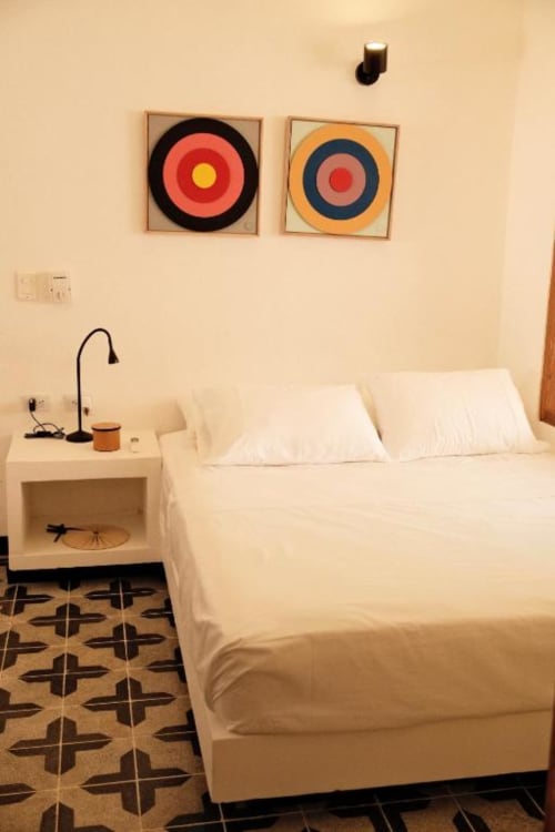 Dormitorio minimalista en Seaflower boutique lodge con cama blanca, arte geométrico colorido en pared, mesita de noche con lámpara, decoración con patrones