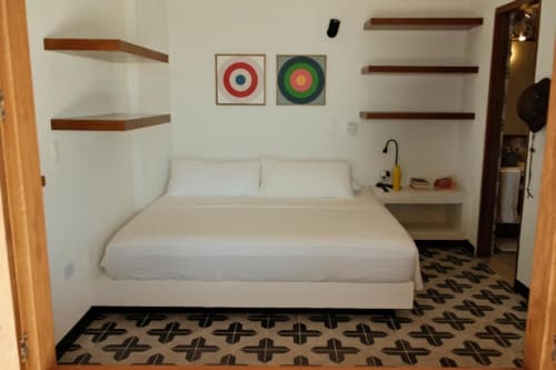 Dormitorio de la boutique hotel Seaflower con cama blanca, estantes de madera, piso con patrón geométrico y arte mural colorido en San