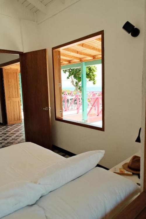 Habitación luminosa en la boutique lodge Seaflower con vista al mar a través de puerta y ventana turquesas que dan a terraza rosa
