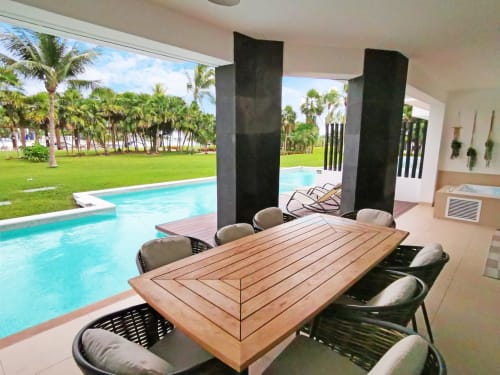 Área de comedor frente al mar en Mareazul Resort Playa del Carmen con vista a la piscina, mesa de madera, sillas modernas y palmeras