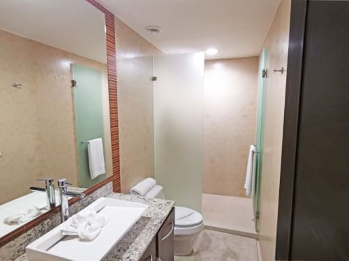 Baño moderno del Resort Mareazul frente al mar con encimera de granito, lavabo de cerámica, inodoro y ducha con cabina de cristal