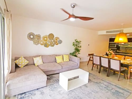 Sala moderna en Mareazul Resort Beachfront con sofá seccional gris, acentos amarillos y comedor en Playa del Carmen
