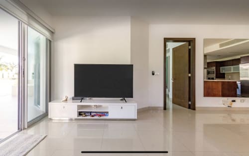 Sala moderna con televisor de pantalla plana, consola blanca y vista al jardín en Mareazul Condo el Cielo, Playa del