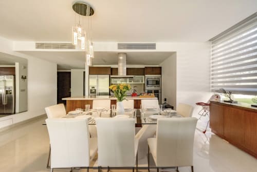 Comedor moderno con sillas blancas y mesa de madera con vista a la cocina en departamento Mareazul Playa del Carmen