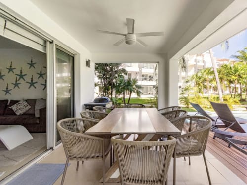 Comedor en terraza cubierta de Mareazul Resort con mesa de madera, sillas tejidas, vista al océano, ventilador de techo y jardín tropical