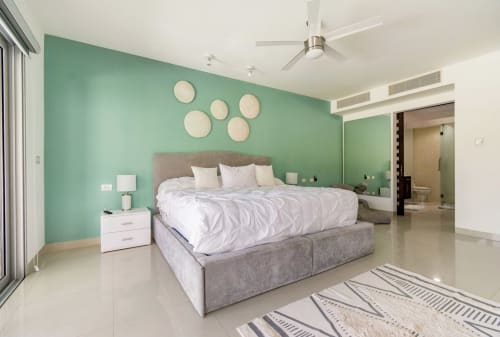 Moderna recámara en Mareazul Condo el Cielo, Playa del Carmen, con pared de acento verde menta, cama gris y acceso a vista del jardín