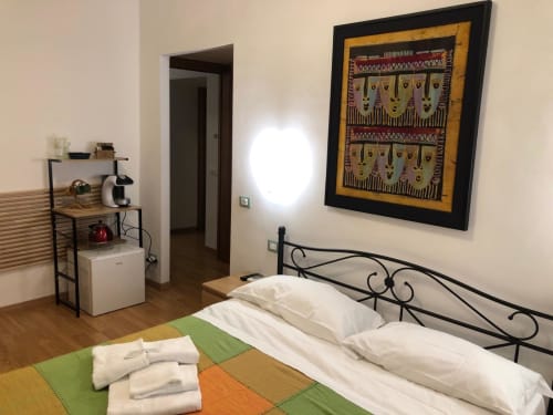 Double Room D1 at Maison Vaticana Guest House Rome with bed, desk, mini-fridge, and African-inspired wall art on wooden floor