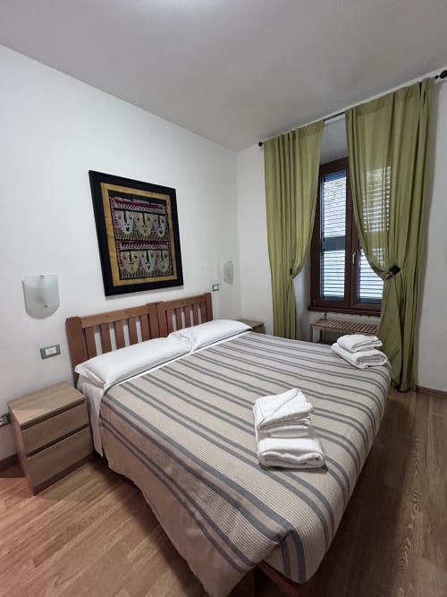 Double room at Maison Vaticana Guest House Rome with wooden bed, striped bedding, green curtains, and framed artwork