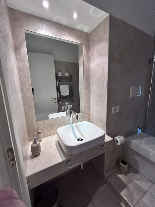 Modern bathroom at Maison Vaticana Guest House Rome with white vessel sink, mirror, shower, and neutral tile finishes