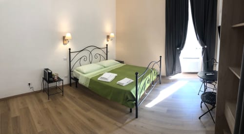 Spacious double room at Maison Vaticana Guest House Rome with iron bed, green bedding, wall sconces, wooden floor, and large