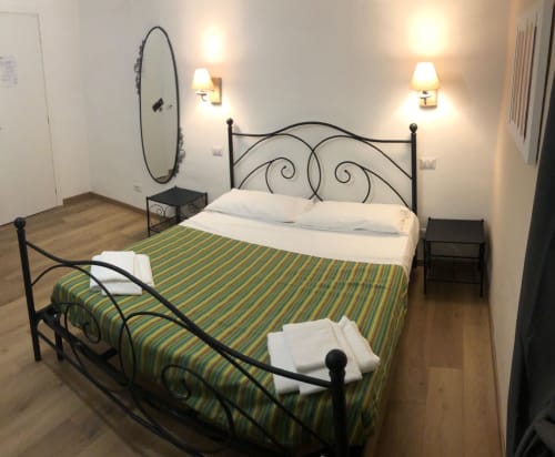 Double bed room at Maison Vaticana Guest House Rome with striped bedding, wrought iron headboard, wall sconces, and round
