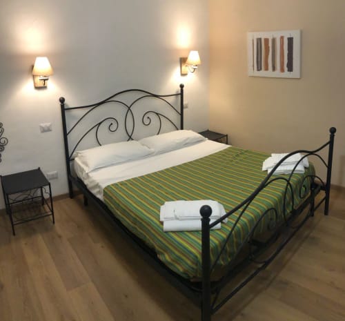 Double bed with green striped bedding and white pillows in Rome guest house room with black metal headboard and wall sconces