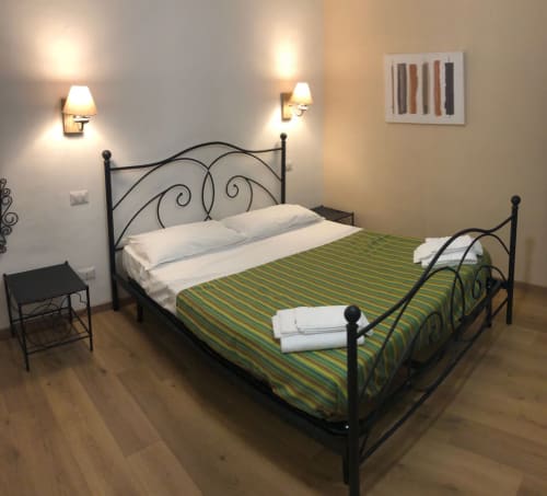 Elegant double bedroom at Maison Vaticana Rome with wrought iron bed, green striped bedding, wall sconces, and modern