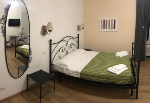 Maison Vaticana Rome double room with wrought iron bed, green striped bedding, ornate mirror, wall sconces, and wood flooring