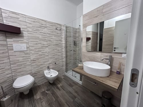 Modern bathroom in Maison Vaticana Rome with gray tile, white basin, toilet, walk-in shower and vanity mirror