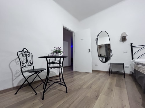 Modern guest room at Maison Vaticana Rome with black wrought iron furniture, ornate mirror, and wood flooring