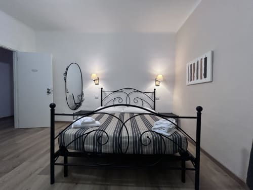 Modern bedroom at Maison Vaticana Guest House Rome with black metal bed, striped bedding, wall sconces, and contemporary