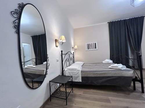 Elegant double bedroom at Maison Vaticana Guest House Rome with black ornate mirror, striped bed, dark curtains