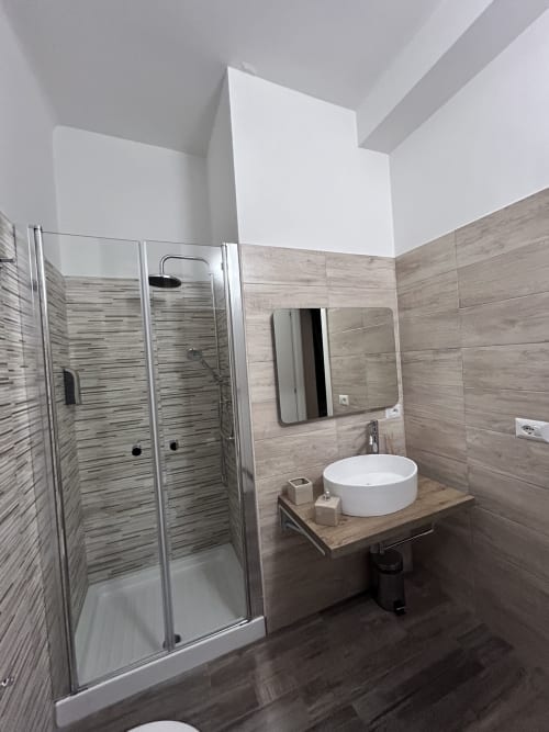 Modern bathroom at Maison Vaticana Rome with walk-in shower, round white sink, wood-grain tile walls, and contemporary