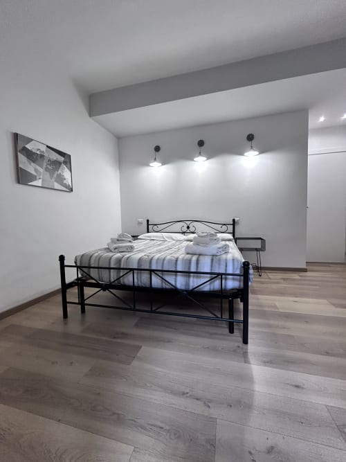Modern bedroom at Maison Vaticana Guest House Rome with black metal bed, striped mattress, wooden floors, and pendant