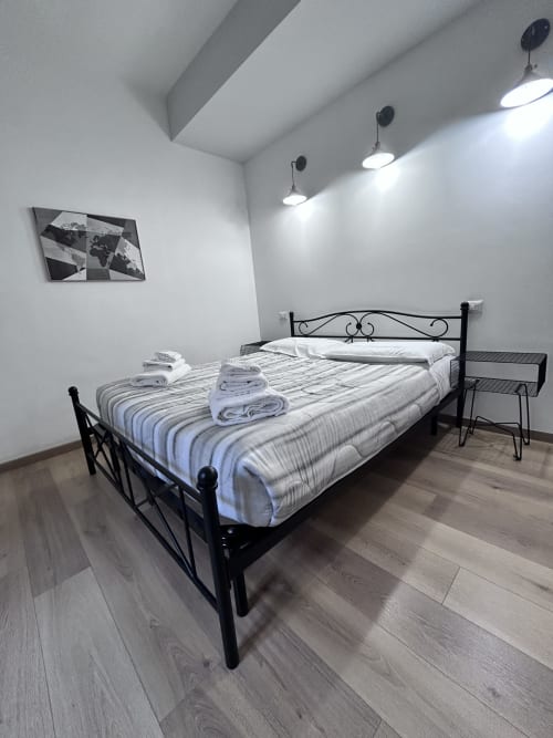 Modern bedroom in Maison Vaticana Rome with black metal bed frame, striped bedding, pendant lights, and minimalist decor