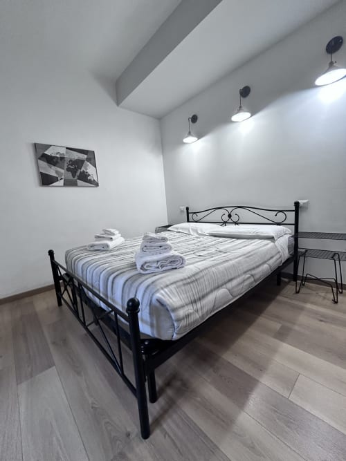 Modern bedroom at Maison Vaticana Guest House Rome with black metal bed, striped bedding, white walls, pendant lights, and