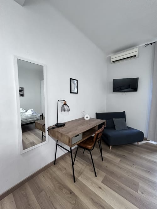 Modern studio suite at Maison Vaticana Rome with wooden desk, black sofa, TV, mirrored closet, and air conditioning