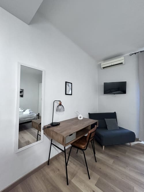 Modern suite at Maison Vaticana Rome with wooden desk, black sofa, TV, and ensuite bedroom view