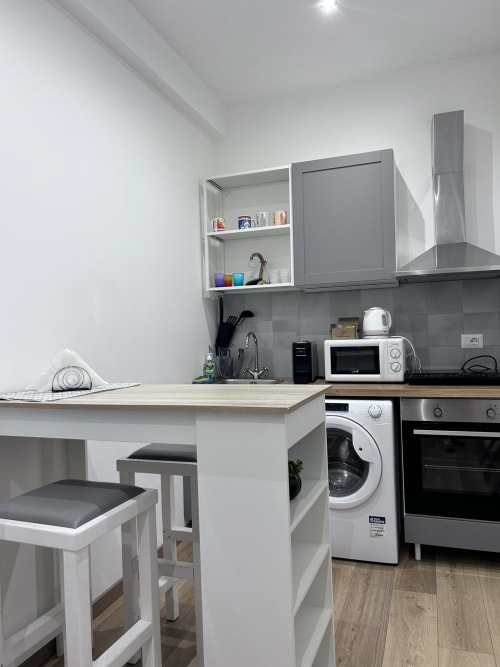 Modern kitchen in Maison Vaticana Rome suite with white cabinetry, stainless steel appliances, and bar seating