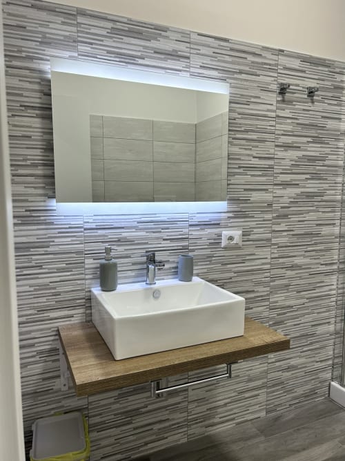 Modern bathroom vanity with white sink, wooden countertop, and striped tile wall at Maison Vaticana Rome