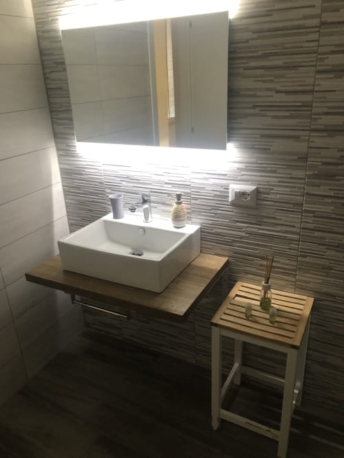 Modern bathroom in Maison Vaticana Rome with white vessel sink, striped tile walls, lit mirror, and wooden stool