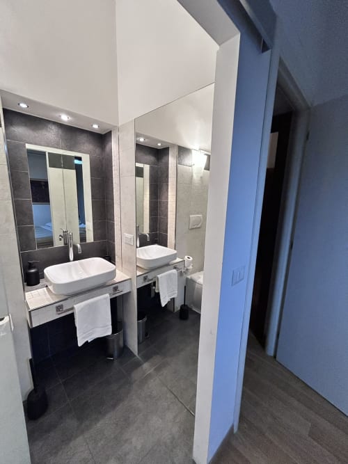 Modern bathroom in Maison Vaticana Rome with dual white vessel sinks, large mirrors, dark tile flooring, and contemporary