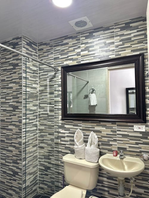 Baño moderno del Hotel Maderos Cali con azulejos rayados, lavabo doble, espejo enmarcado y ducha abierta.
