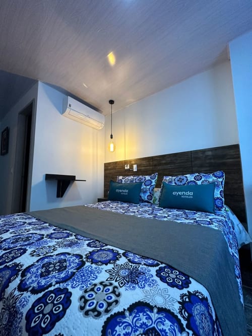 Habitación moderna del Hotel Maderos Cali con ropa de cama azul estampada, cabecera oscura, aire acondicionado e iluminación colgante