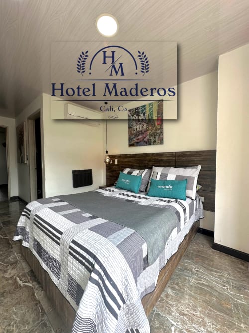 Habitación del Hotel Maderos Cali con cama queen, ropa de cama a rayas, almohadas turquesas, cabecero de madera oscura y pared decorativa