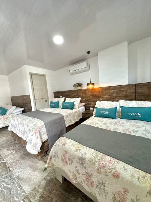 Moderna habitación del Hotel Maderos Cali con múltiples camas, almohadas turquesas, cabecero de madera y techo blanco brillante
