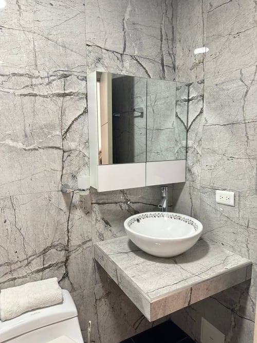 Baño moderno del Hotel Maderos Cali con paredes de mármol, lavamanos tipo recipiente y espejo con gabinete