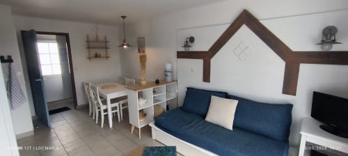 Appartement moderne à Loc'Maria Belle Île avec canapé bleu, table à manger et cuisine ouverte, vue sur le jardin