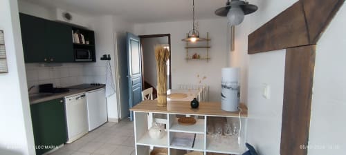Cuisine et salle à manger modernes de l'appartement Loc'Maria, Belle Île en Mer, avec table en bois, rangements ouverts et touches de vert