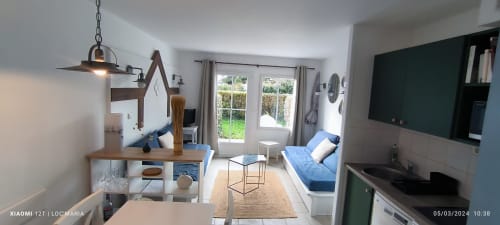 Appartement moderne à Loc'Maria Belle Île en Mer avec lit bleu, kitchenette, télévision et vue sur le jardin par les portes-fenêtres