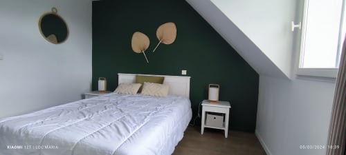 Chambre moderne avec lit blanc, mur d'accent vert, deux ventilateurs décoratifs, table de nuit avec bougie et fenêtre de toit