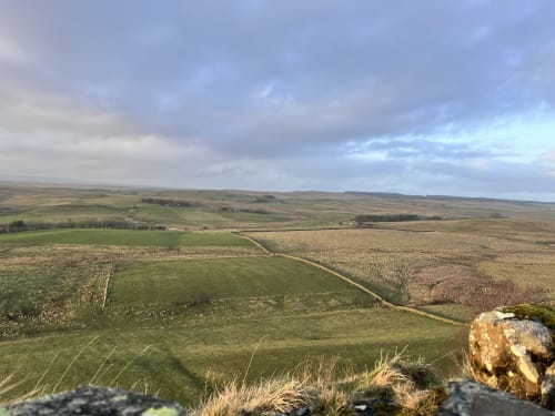 Rolling countryside landscape near Haydon Bridge with green fields, stone outcrops, and distant hills under cloudy skies