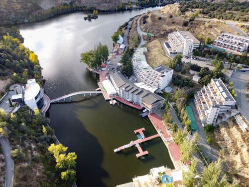 Hotel Náyade in Segovia overlooks a river with modern architecture, terraces, and surrounding forested landscape.
