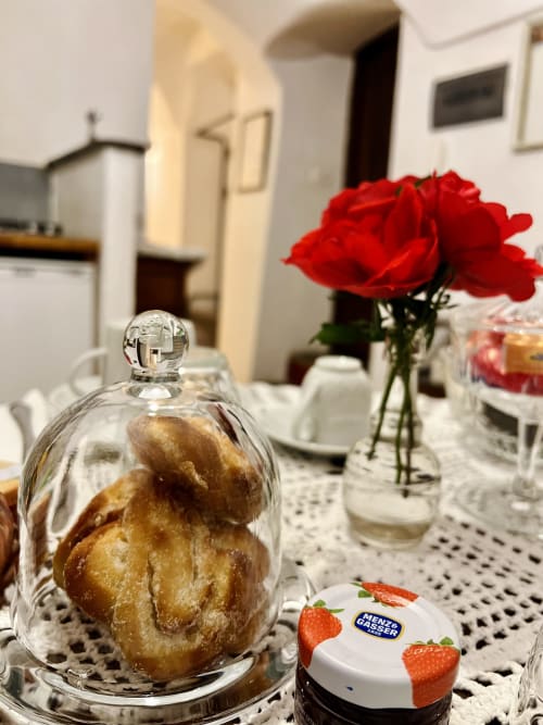 Table de petit-déjeuner élégante à l'Agritusmo Stecadò avec rose rouge, pâtisseries sous cloche et beurre Menzel Gassler