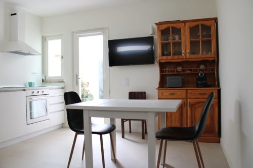 Cozinha moderna integrada à sala de jantar do apartamento Estudio Hortas em Bordeira, com armários brancos, mesa de jantar, cristaleira de madeira e