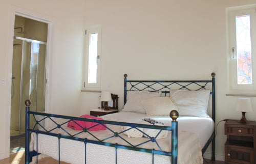 Quarto luminoso com cama de metal, vista para as montanhas pelas janelas e acesso à casa de banho no Estudio Hortas