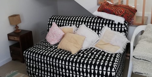 Aconchegante sala de estar de estúdio com sofá estampado em preto e branco, almofadas coloridas, mesa lateral de madeira com luminária e
