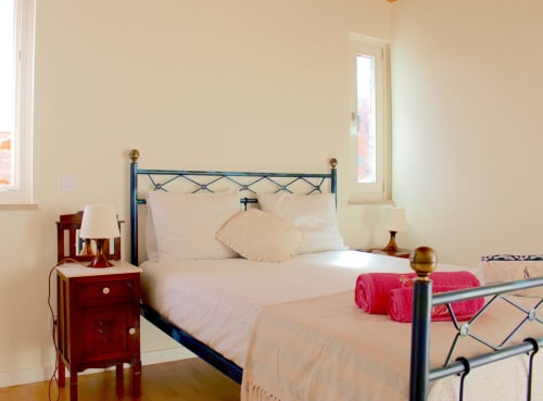 Bright bedroom in Estudio Hortas apartment, Bordeira, with blue metal bed frame, cream bedding, red nightstand, and mountain