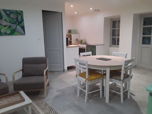 Área de comedor de la casita en Château De Clusors con mesa blanca, sillas, sillón gris y acceso a la cocina