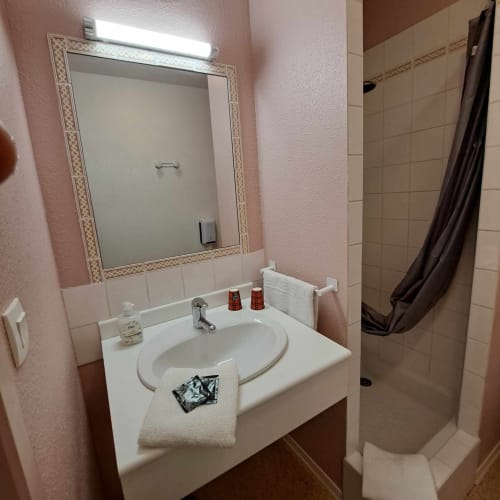 Salle de bain de l'hôtel Les Deux Porches à Verrières avec murs roses, lavabo blanc, miroir encadré et douche